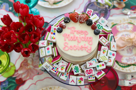 Picture of cake with Troop Mahjong Society written on it in pink surrounded by colorful mahjong tiles.