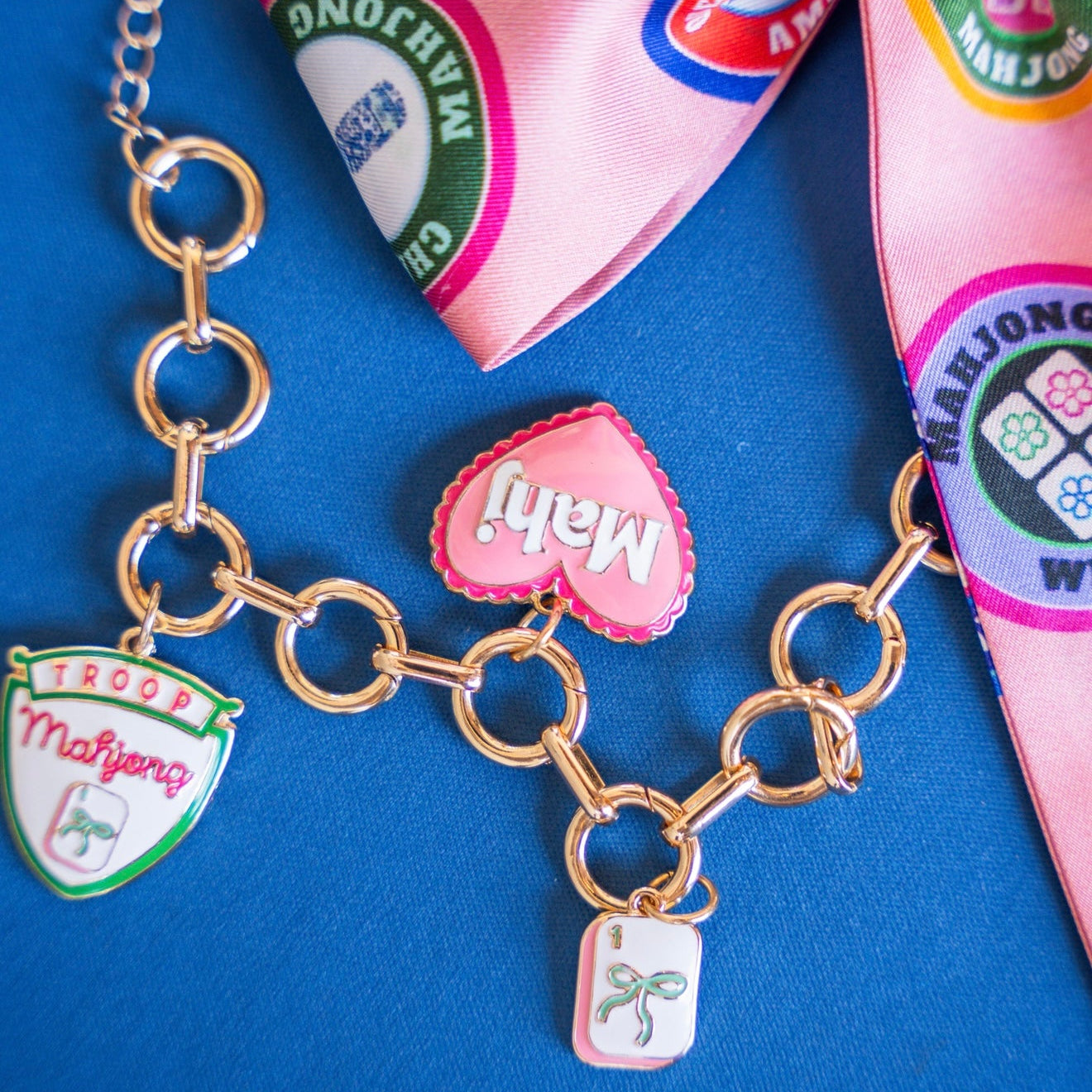 Gold chain bracelet with charms on a blue background with Mahjong-themed items.